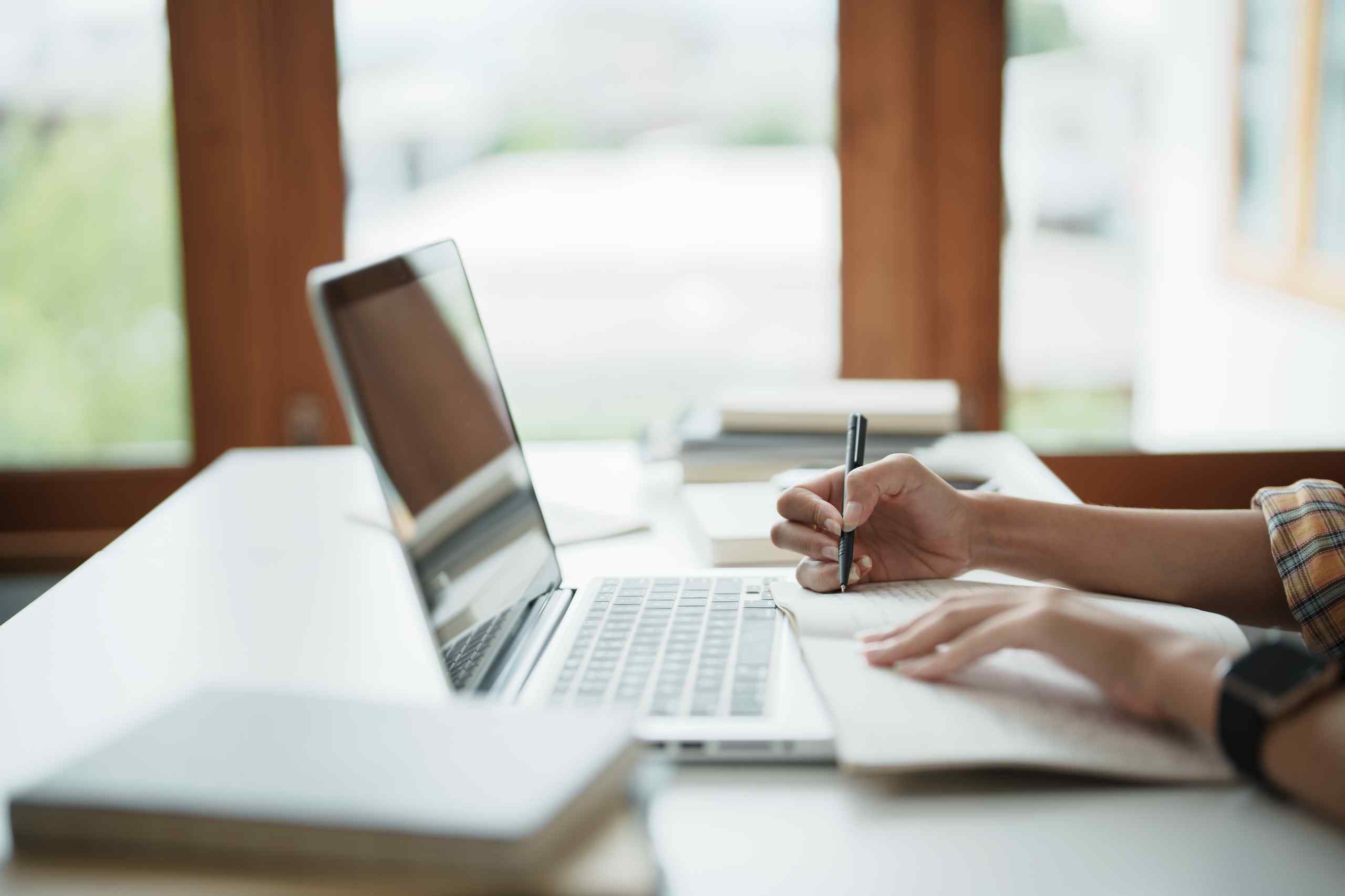A photo of a laptop and someone taking notes.